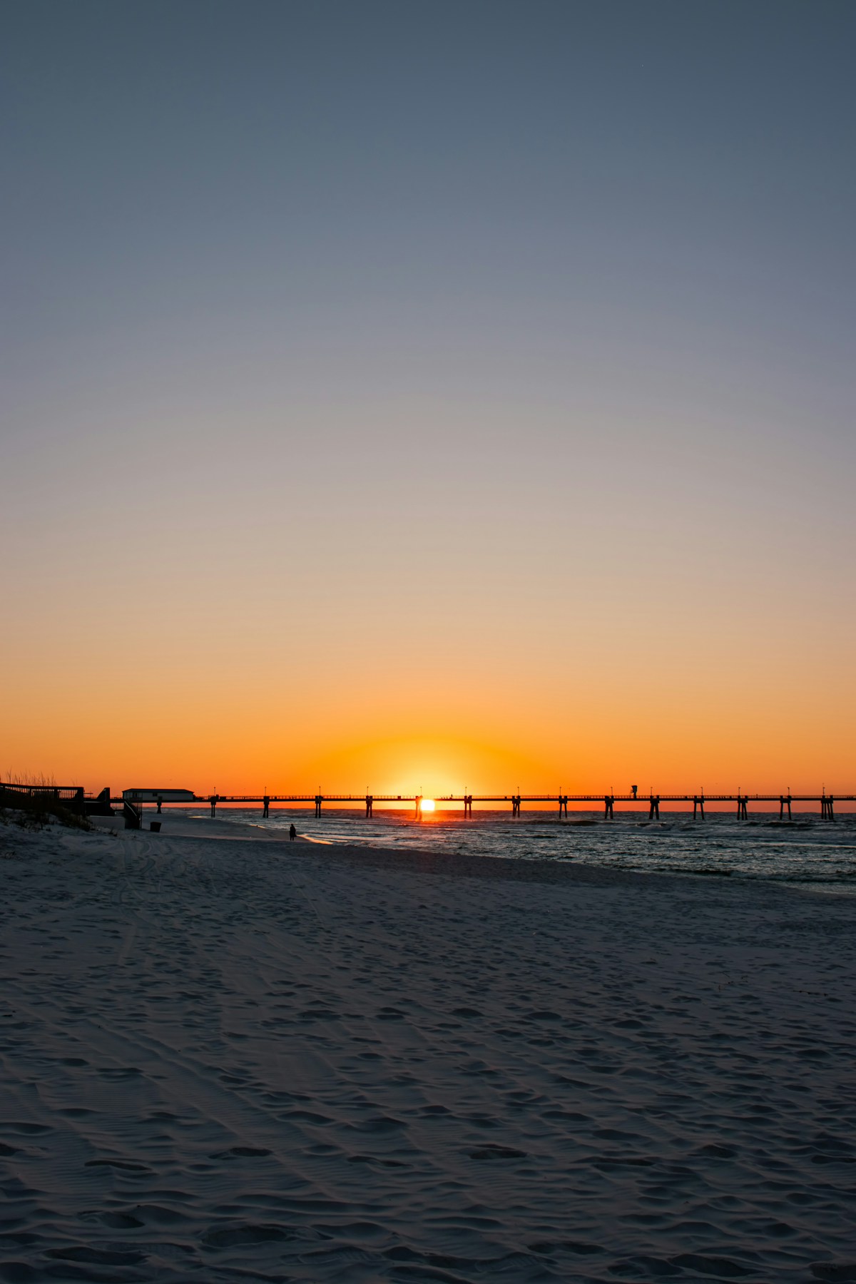 Beach pier silhouetted against a golden sunset over the Gulf waters